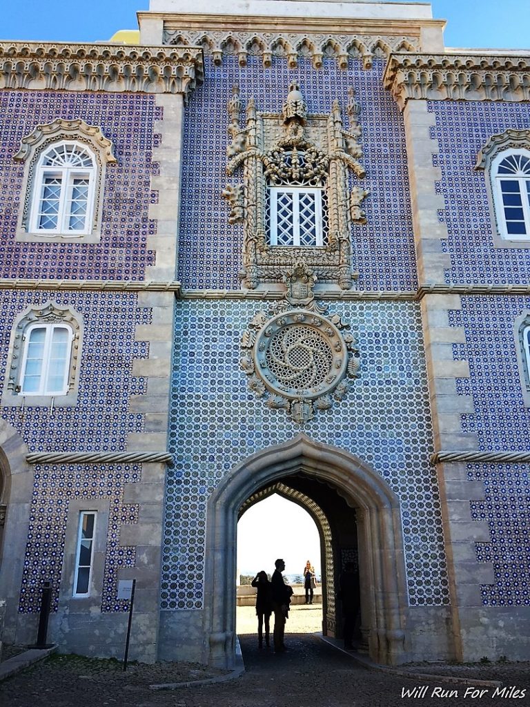 a building with a stone arch and a stone wall with blue tiles