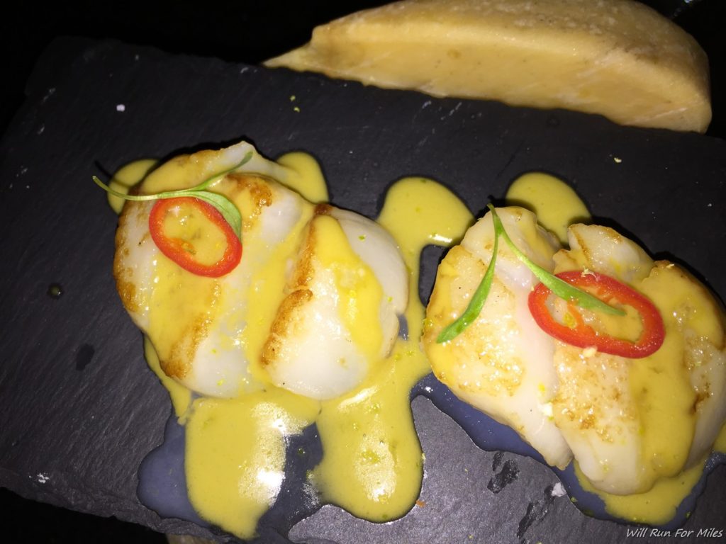 scallops with sauce on a black plate with cheese on it