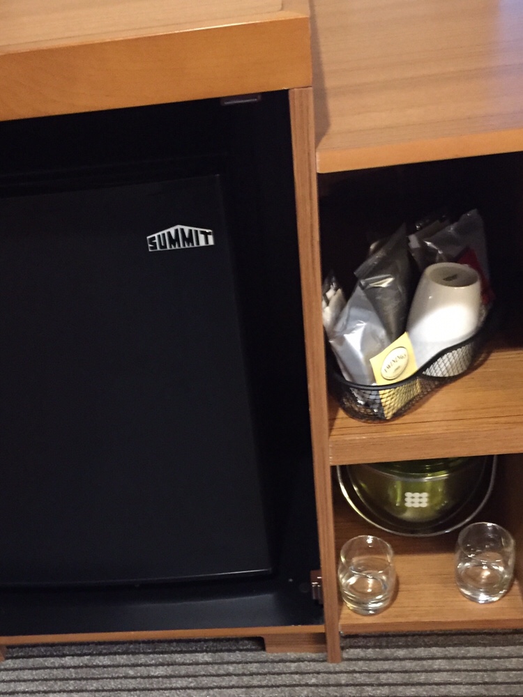 a black refrigerator with a basket of food and glasses on a shelf