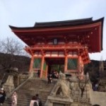 a red pagoda with people walking up stairs with Kiyomizu-dera in the background
