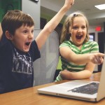 a boy and girl with their hands up in front of a laptop