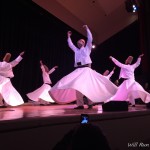 a group of men wearing white dresses dancing on a stage