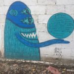 a blue monster painted on a white brick wall