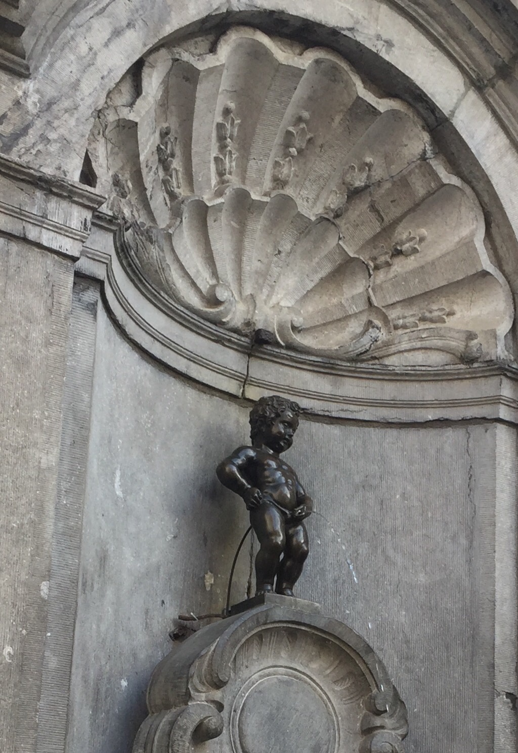 a statue of a baby on a stone wall with Manneken Pis in the background