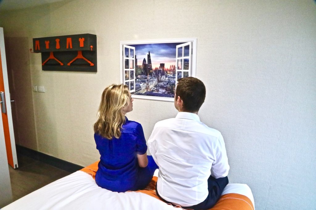 a man and woman sitting on a bed looking at a window