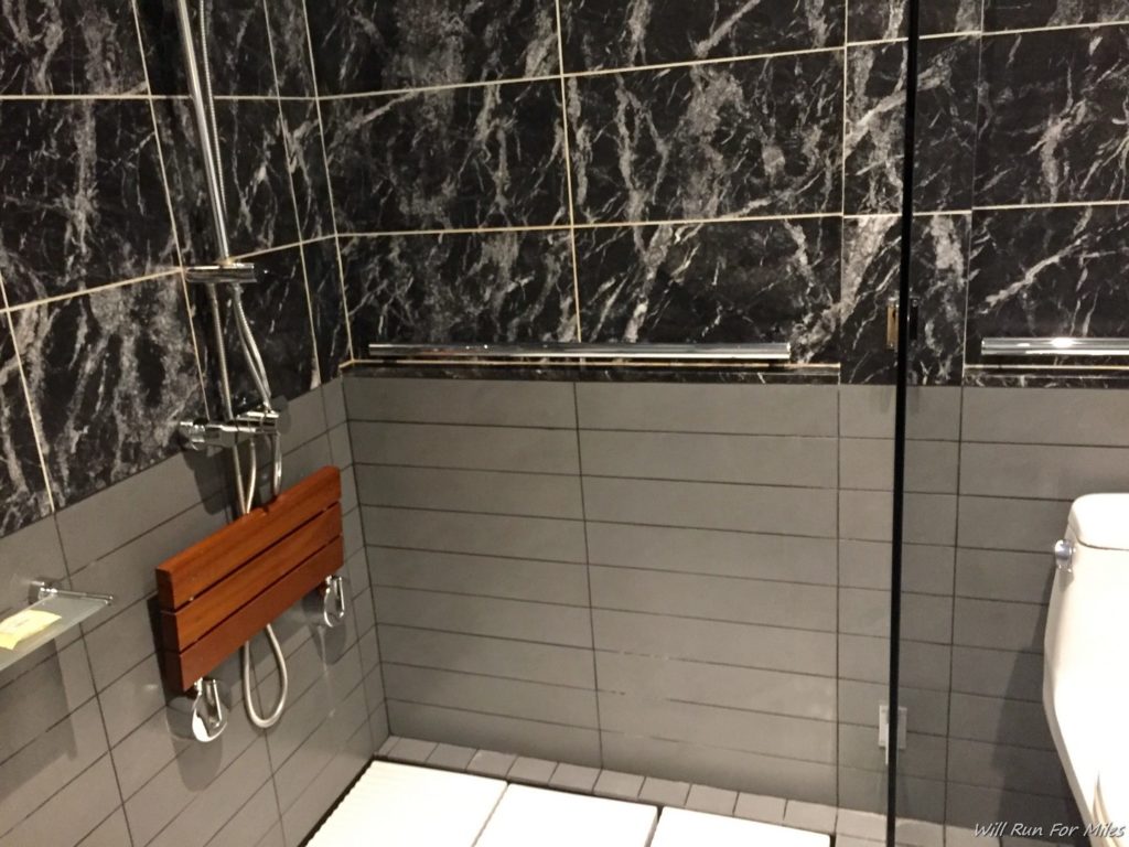 a shower with a wood seat and a shower head