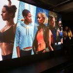 a woman standing in front of a large screen with images of women
