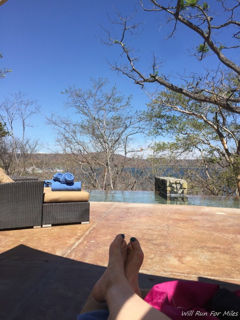 a person's feet on a deck with a pool and trees