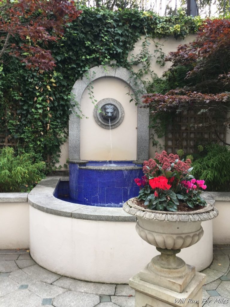 a fountain with a stone wall and a stone urn with a lion head