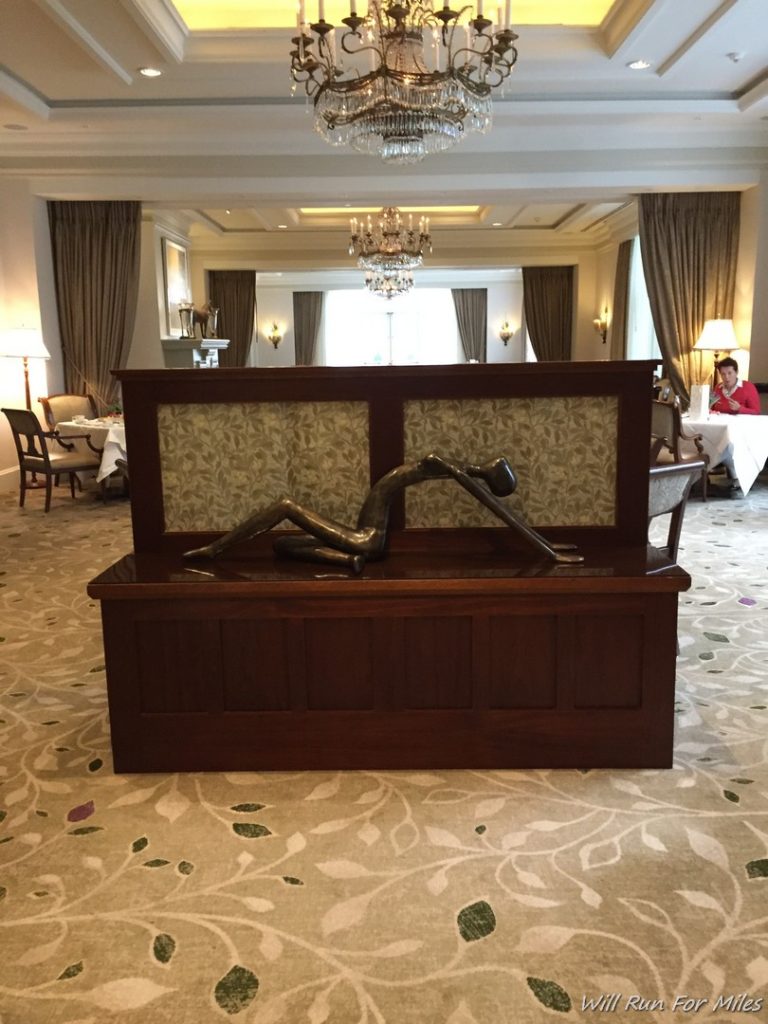 a statue of a person on a bench in a room with chandeliers