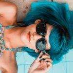 a woman with blue hair lying down and wearing sunglasses