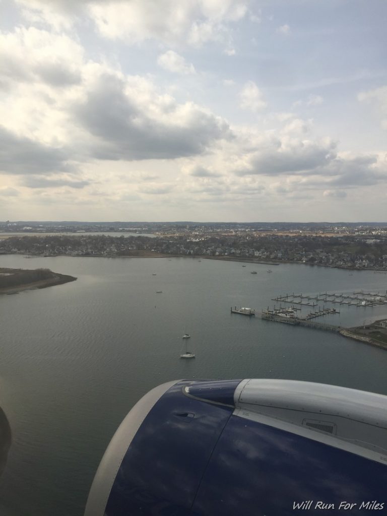 an airplane wing and body of water with boats and a city in the background
