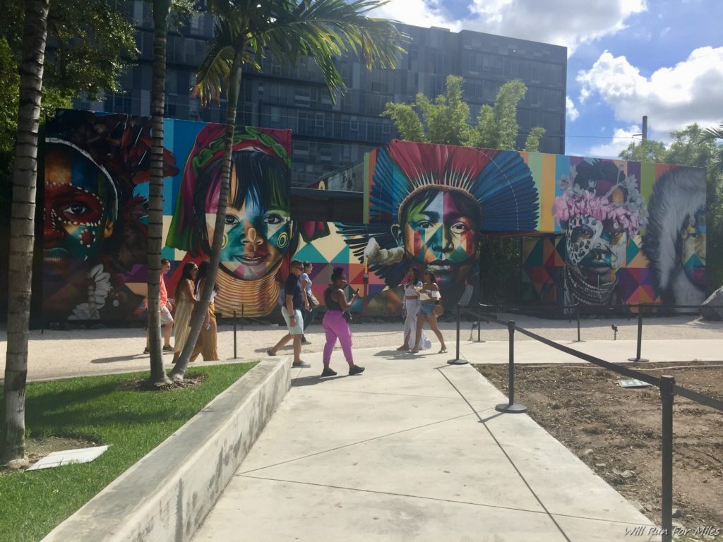 a group of people walking by a building with colorful murals