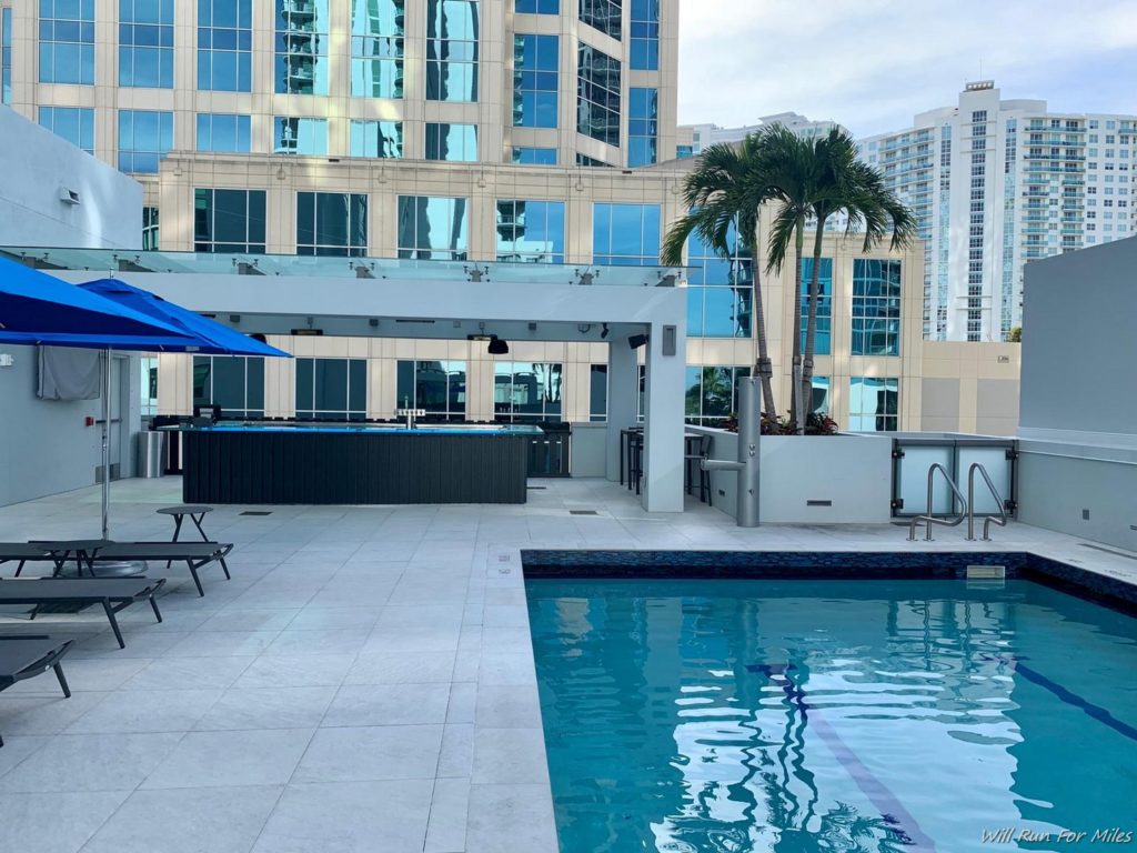 a pool with a blue umbrella and palm trees in front of a building