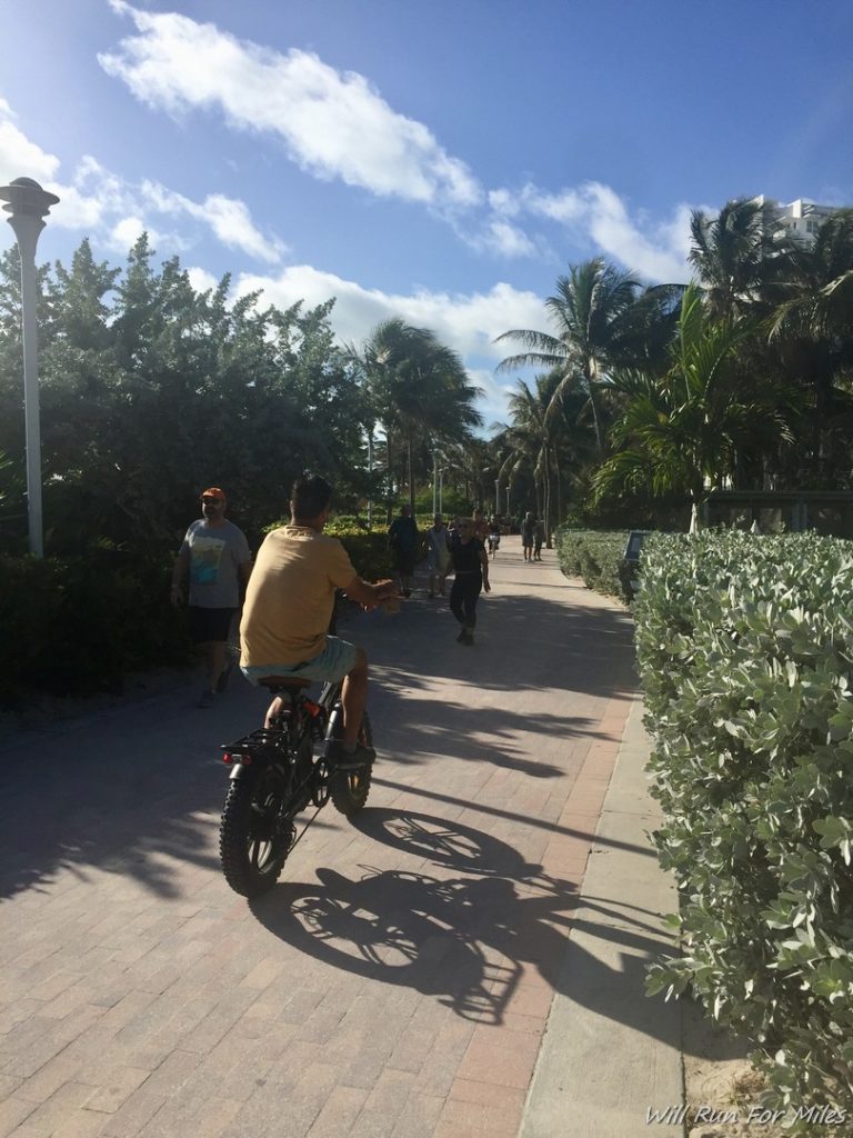 a man riding a bike on a path with trees and people