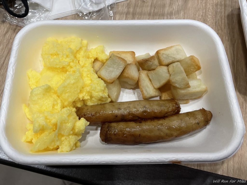 a styrofoam container with sausages and scrambled eggs