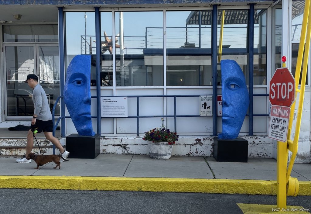 a person walking a dog on a sidewalk next to a blue statue
