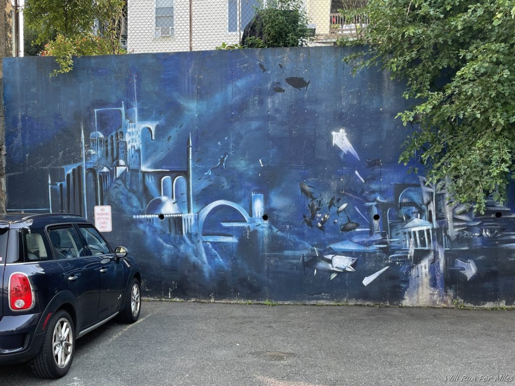 a car parked next to a wall with a painting on it