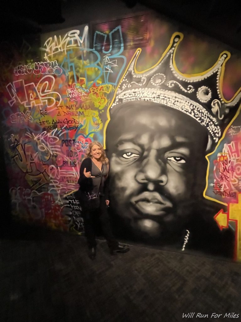 a woman standing in front of a mural of a man and a crown