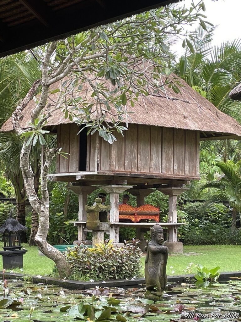 a wooden hut with a thatched roof and a statue in the middle of a garden