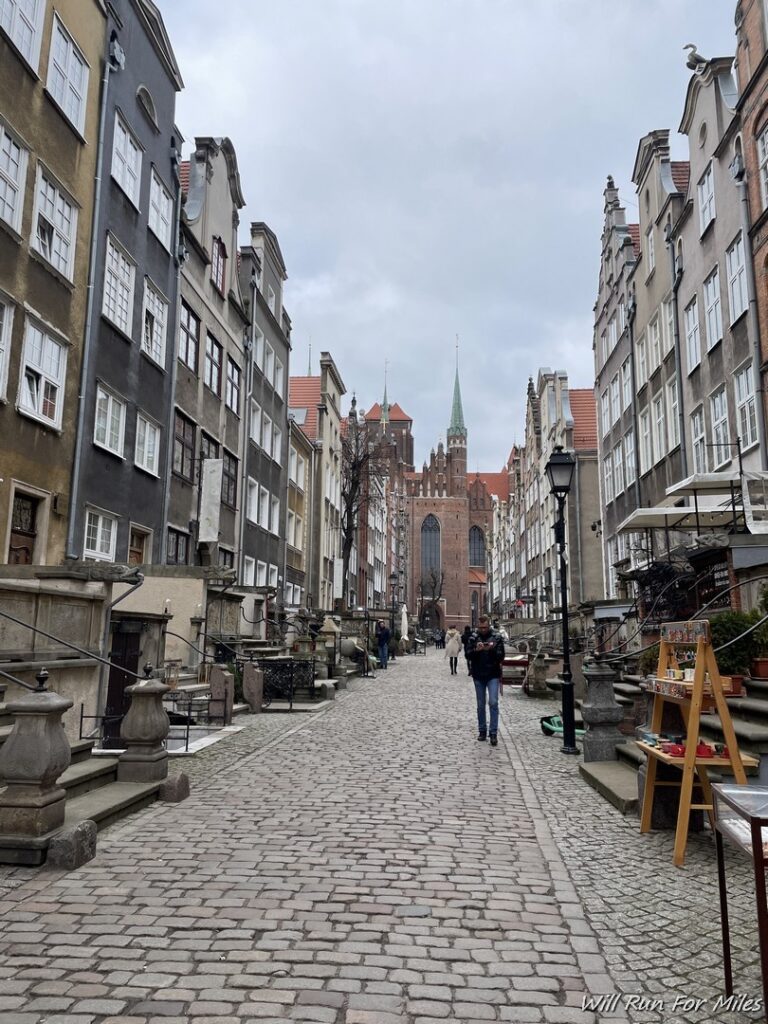 a person walking down a cobblestone street with buildings and a tower