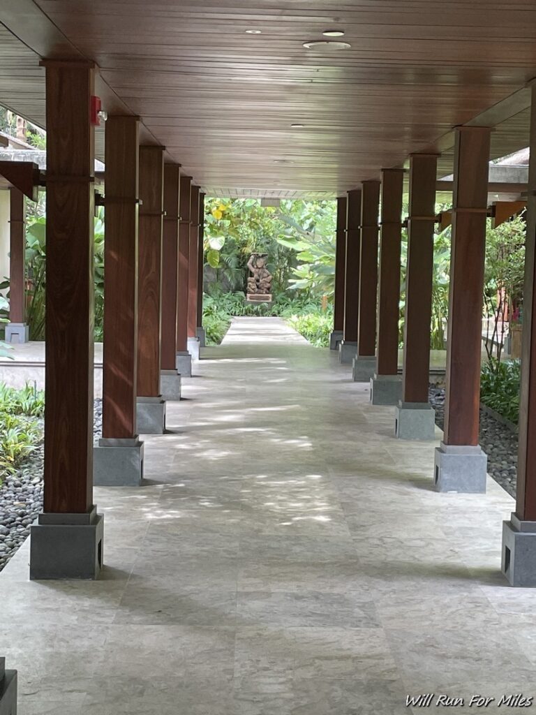 a walkway with pillars and a statue in the background