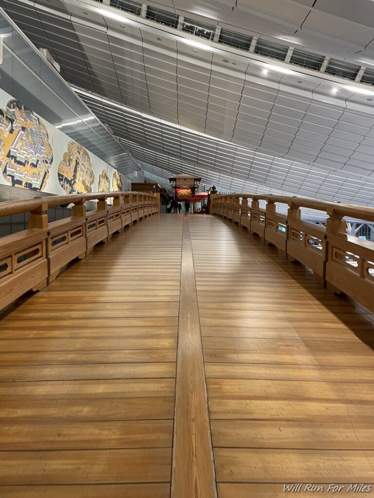 a wooden walkway with railings and a wall of art