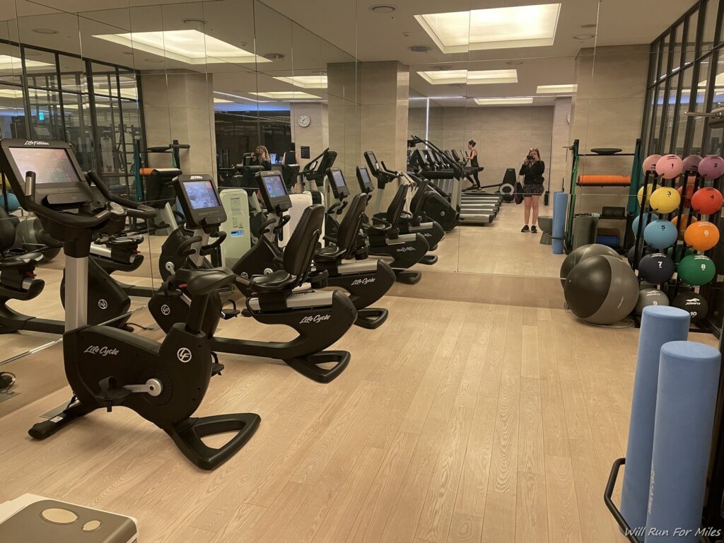 a room with exercise equipment and people walking