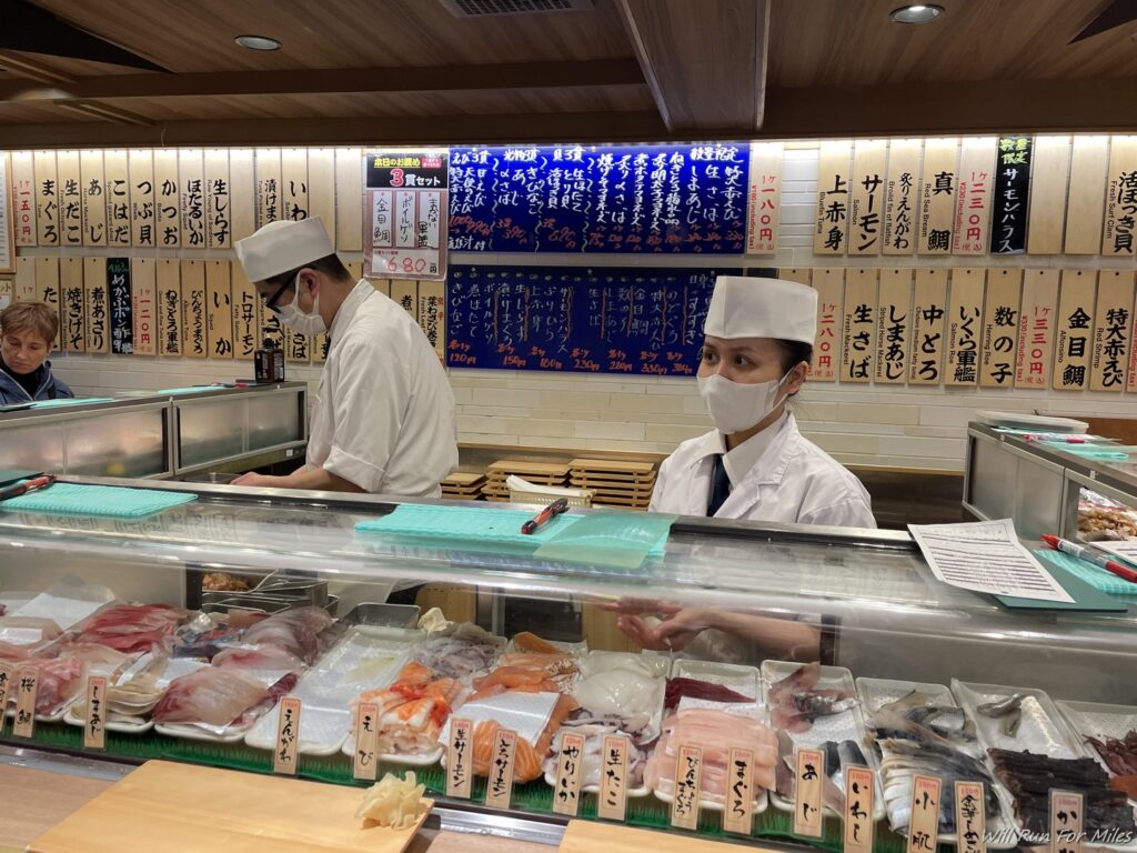 a couple of people wearing masks and standing behind a counter with food