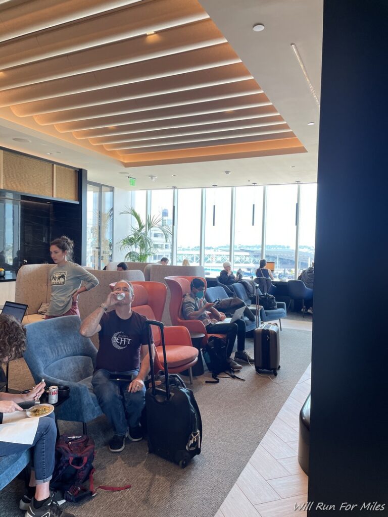 a group of people sitting in a lounge area with chairs and a man with luggage