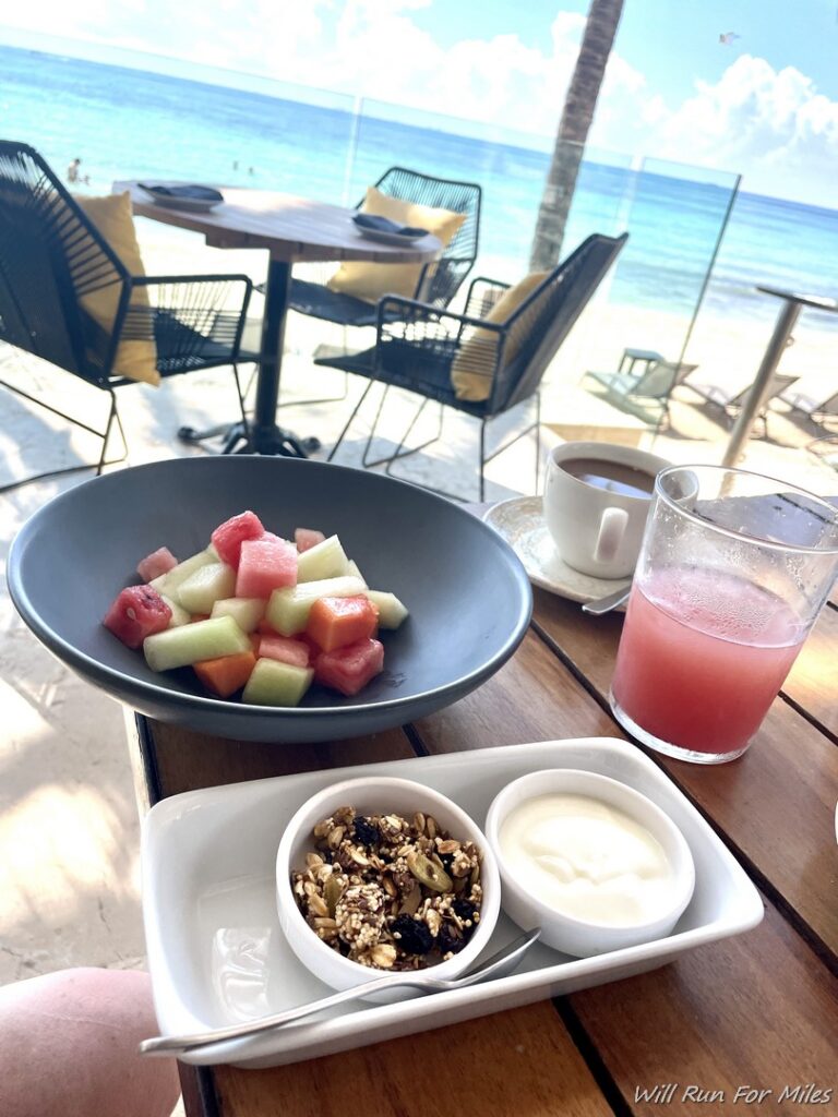 a plate of fruit and yogurt on a table with a beach in the background