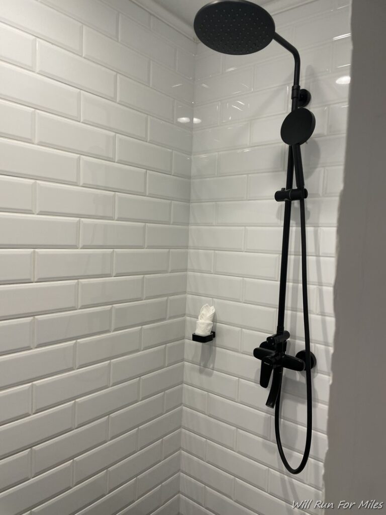 a shower with a black shower head and a tissue paper holder