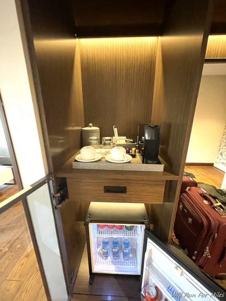 a small cabinet with a small refrigerator and a small table with tea cups and coffee cups