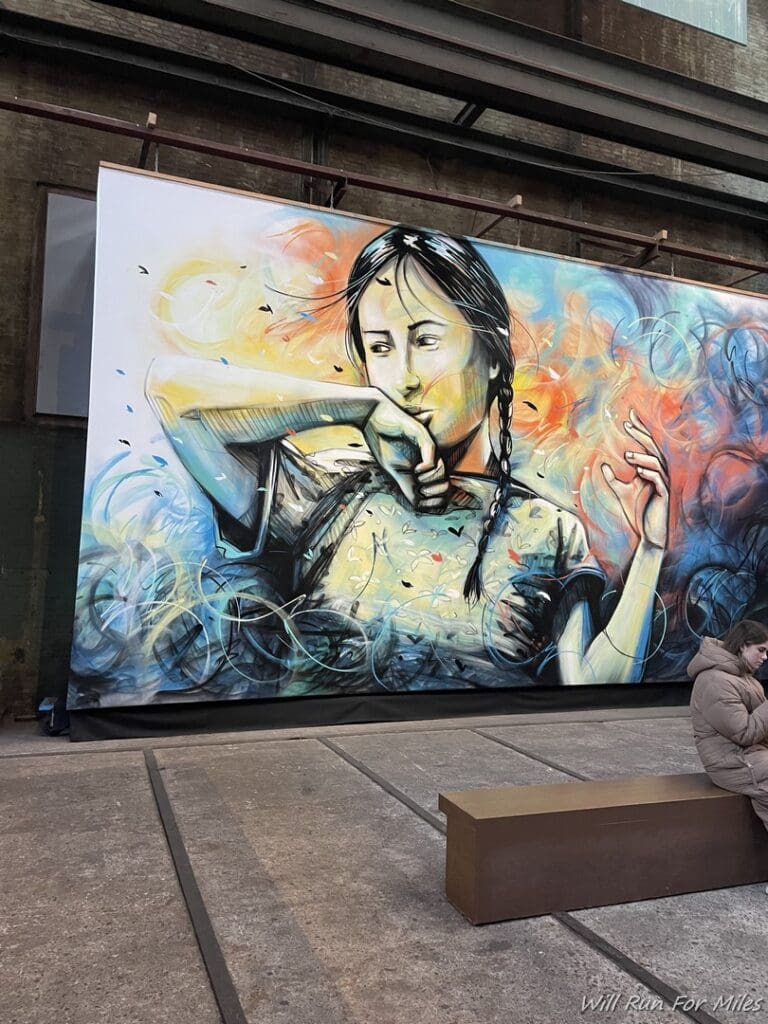 a woman sitting on a bench next to a large mural