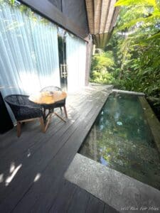 a table and chair on a deck with a pool in the back