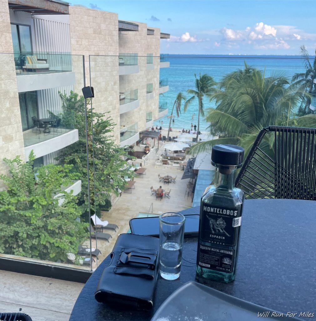 a table with a bottle and glasses on it and a beach in the background