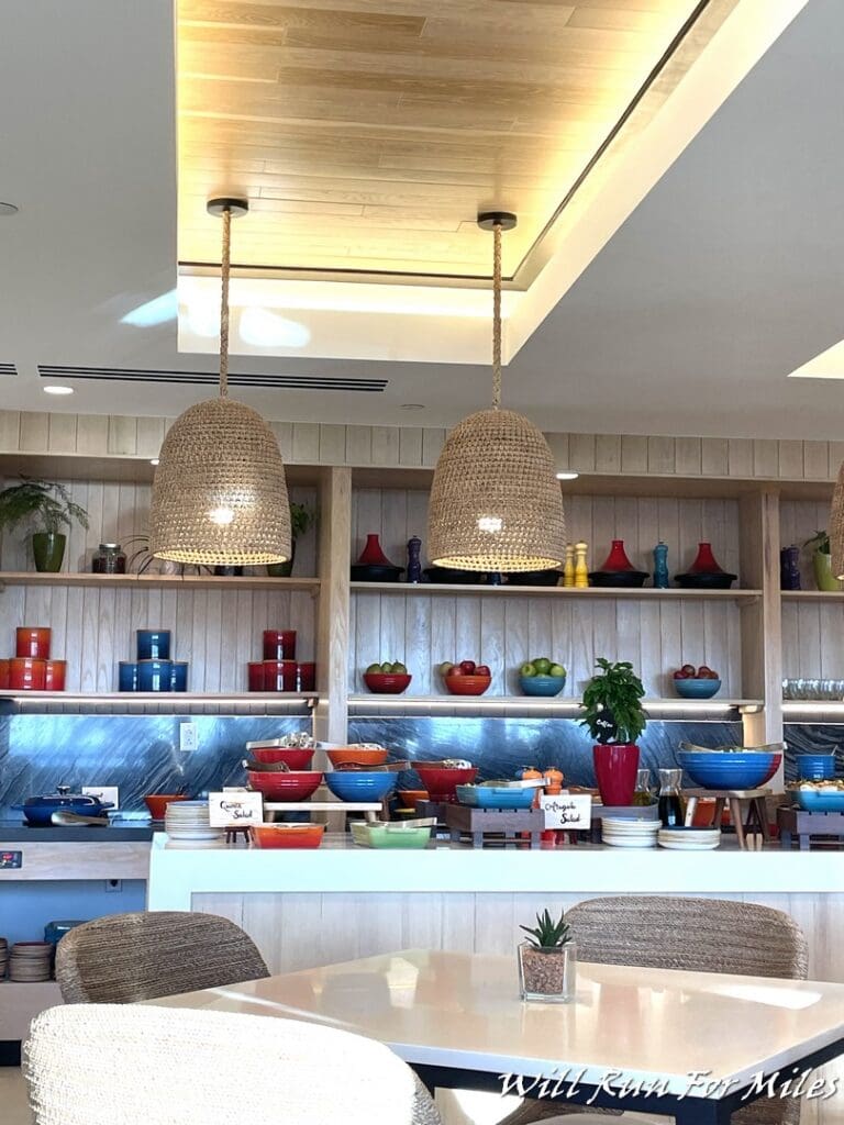 a room with a table and chairs and a table with bowls and a shelf with plants