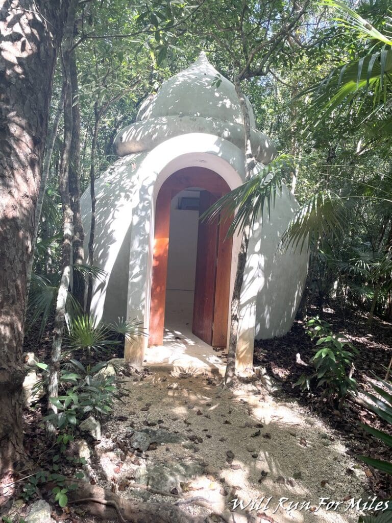 a white round structure with a door in the middle of a forest