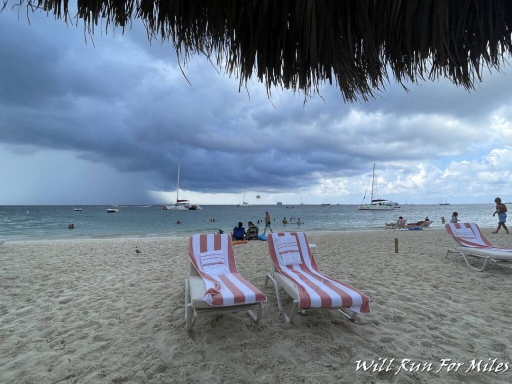 chairs on a beach with a straw roof and people in the water