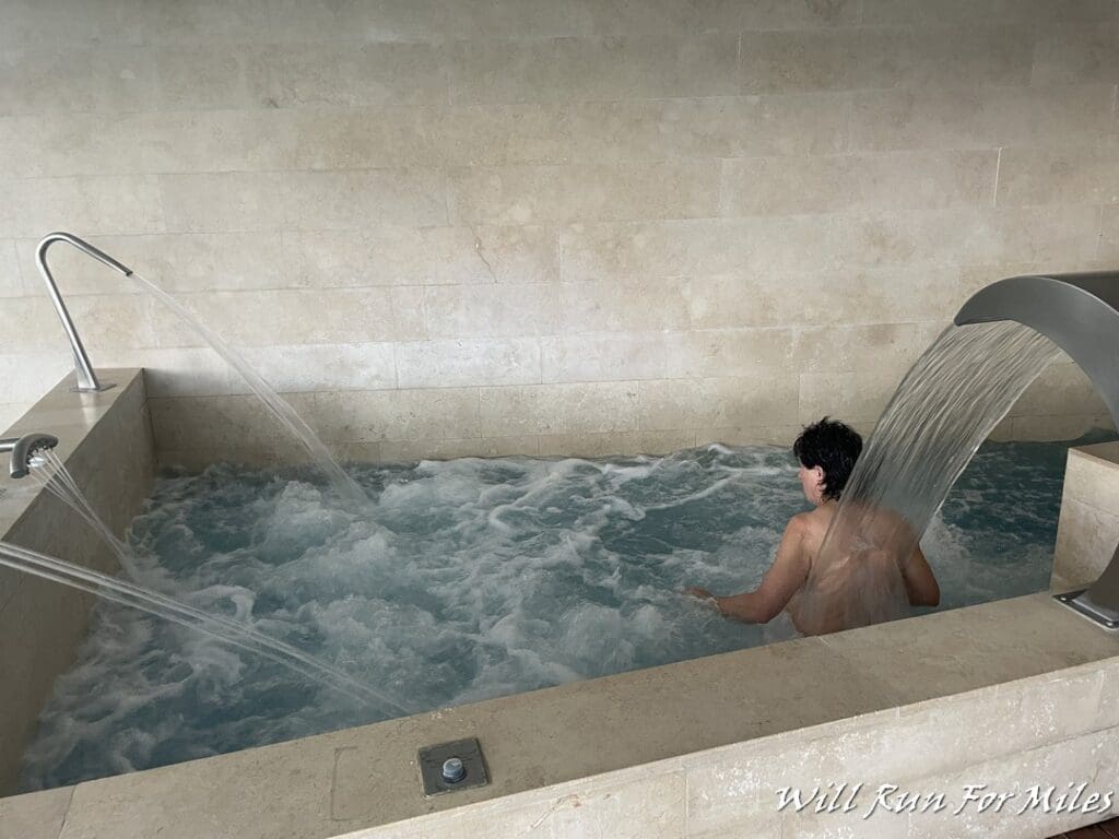 a man in a hot tub with water falling from the top